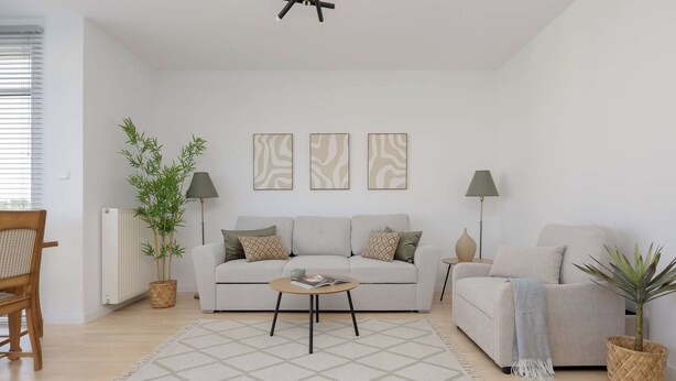 Ein modernes Wohnzimmer mit einer Couch, zwei Sesseln, einem Couchtisch und einer Stehlampe. An den Wänden hängen drei Kunstwerke und es gibt zwei Topfpflanzen.