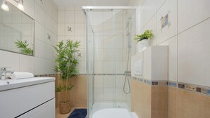 Ein modernes Badezimmer mit Duschkabine aus Glas, Toilette, Waschbecken mit Spiegel und einer Topfpflanze.