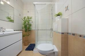 Un baño moderno con cabina de ducha de vidrio, inodoro, lavabo con espejo y una planta en maceta.