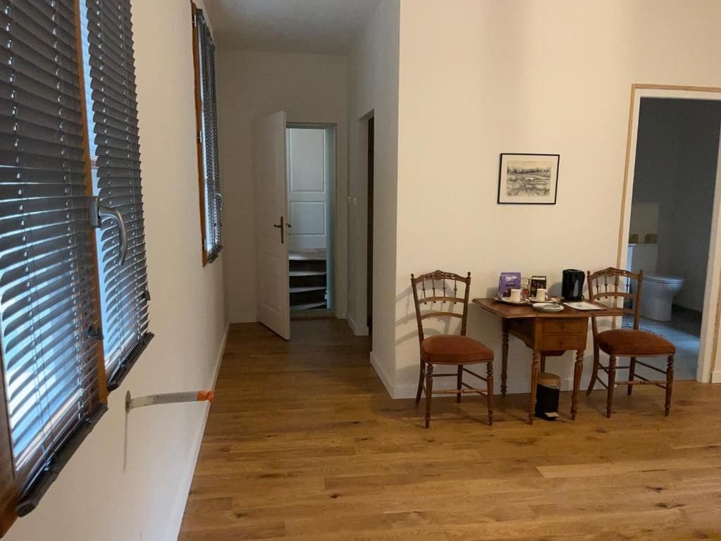 Een eetgedeelte met een houten tafel en stoelen, een ingelijste foto aan de muur, en een deur die naar een andere kamer leidt.