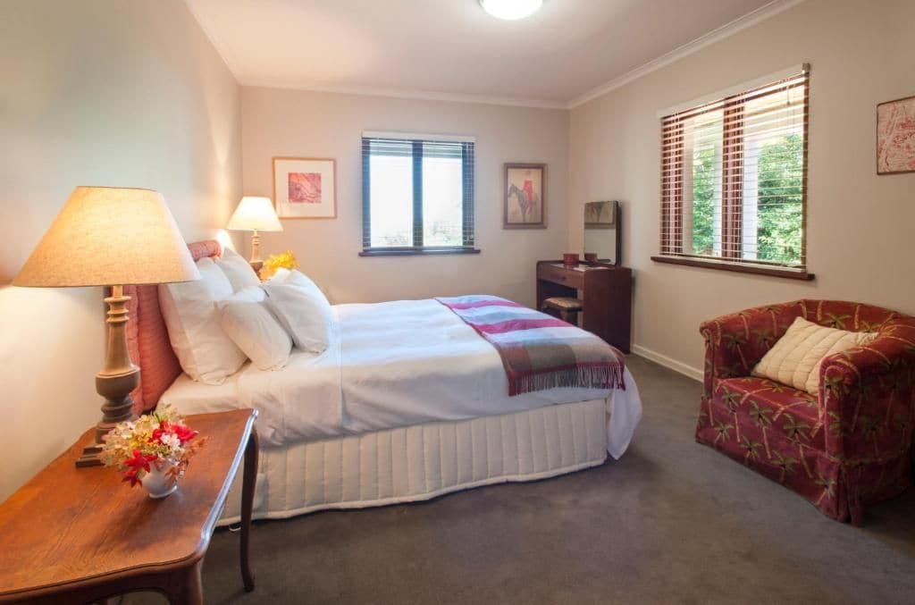 A bedroom with a bed, bedside tables, a chair, a desk, and a window.