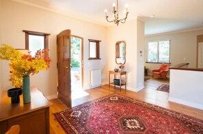 A spacious hallway with a wooden floor, a large rug, a wooden door, and a mirror on the wall.