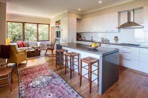 A modern kitchen with a central island, bar stools, and a dining area with a sofa and chairs. - Boyanda (Ferny Creek)
