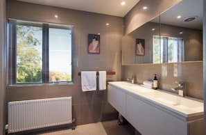 A modern bathroom with a large window, a white radiator, a double sink vanity, and a mirror.
