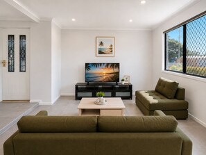 Ein Wohnzimmer mit einem großen Flachbildfernseher, einer Couch, einem Couchtisch und einem Fenster mit Blick.