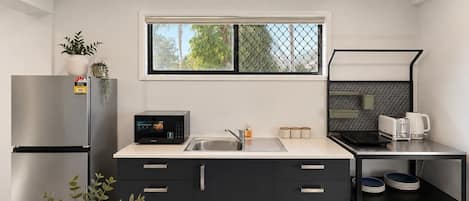A modern kitchen with a stainless steel refrigerator, a microwave, a sink, and a coffee maker. There are cabinets with drawers and a shelf with dishes.