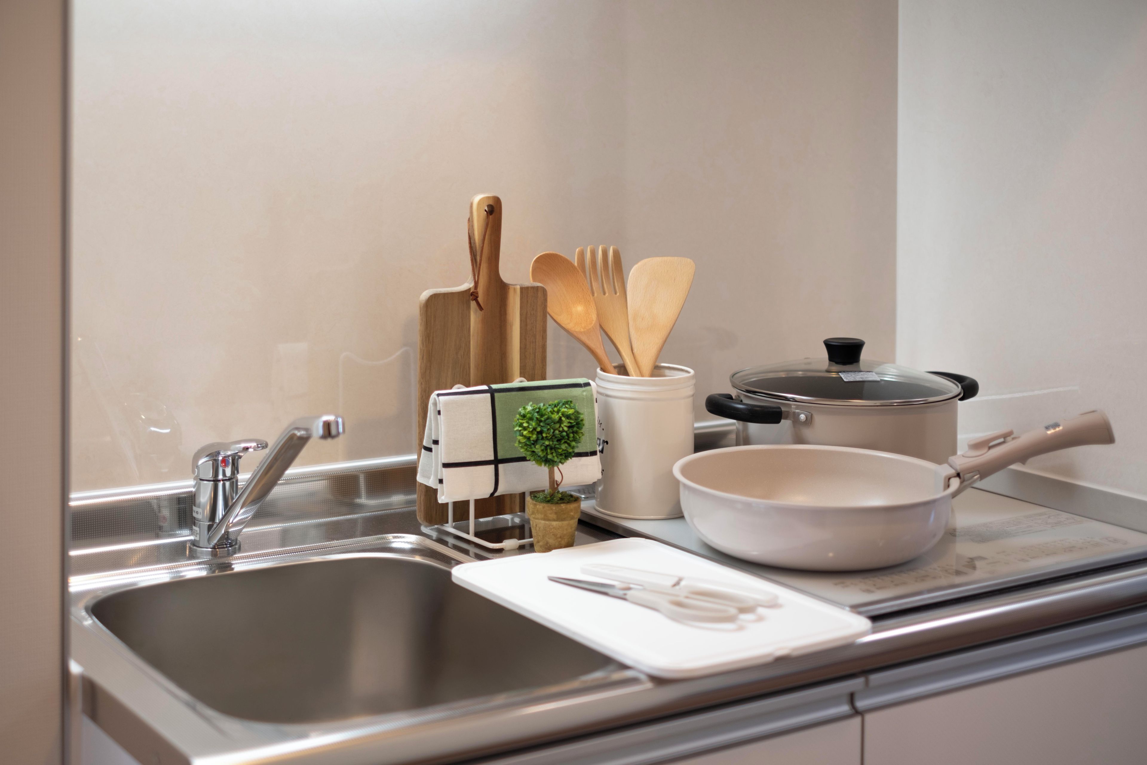 Una cocina con un lavamanos de acero inoxidable, una olla blanca, una sartén blanca y utensilios de madera.