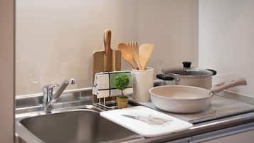 Una cocina con un lavamanos de acero inoxidable, una olla blanca, una sartén blanca y utensilios de madera.