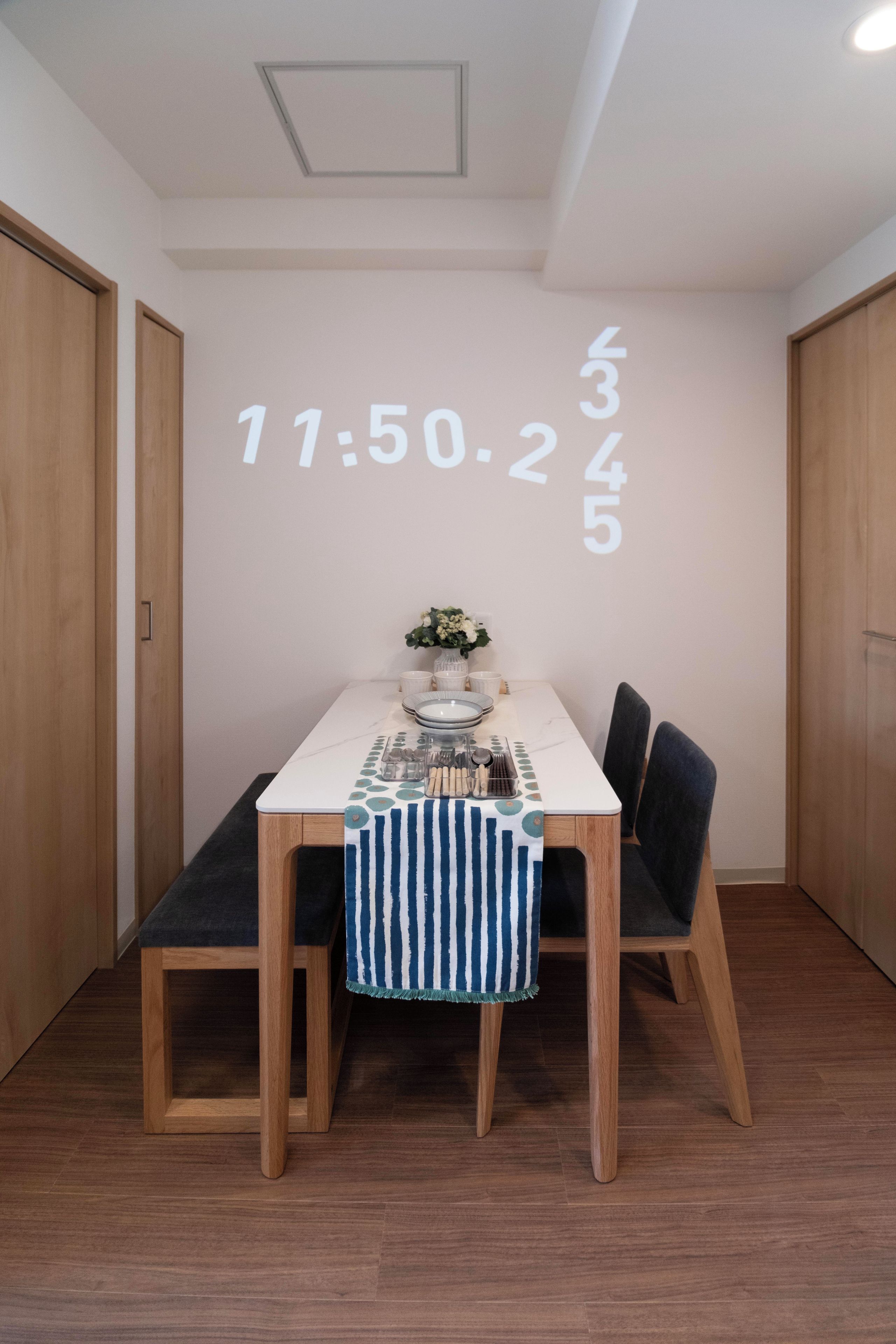A dining area with a table set for two, a clock on the wall, and wooden flooring.