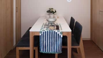 A dining area with a table set for two, a clock on the wall, and wooden flooring.