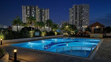 A swimming pool with a surrounding deck, palm trees, and high-rise buildings in the background.