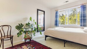 Ein Schlafzimmer mit einem Bett, einem Sessel, einer Pflanze und einem Fenster mit Vorhängen.