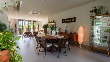 Een ruime eethoek met een ronde tafel, rieten stoelen en een glazen kast met servies.