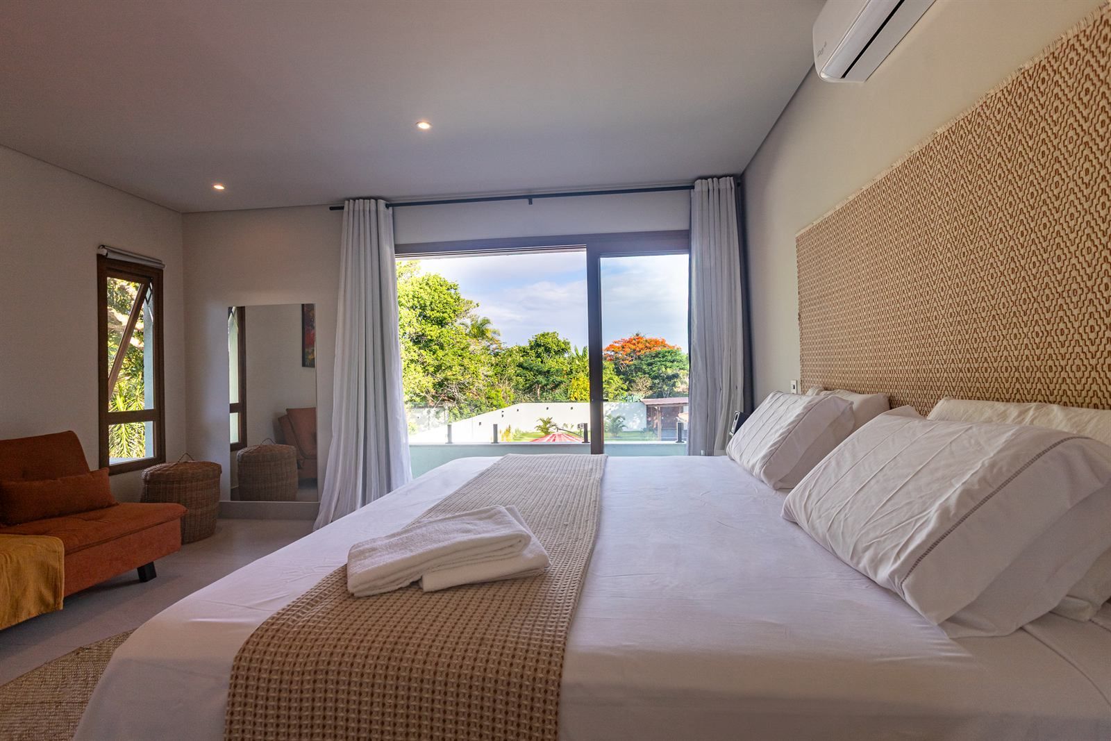 Quarto de hotel com uma cama grande, um sofá, uma poltrona e vista para o exterior.