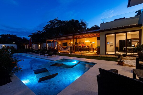 Una casa moderna con piscina, mobiliario exterior y un patio cubierto.