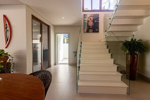 Un interior moderno con una escalera, un comedor y un pasillo que conduce a una puerta de cristal.