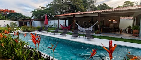 Una piscina con sillones de descanso y un porche cubierto.