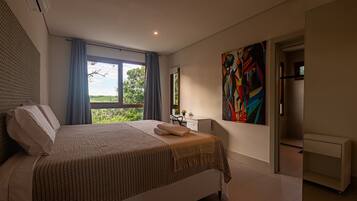 Een moderne slaapkamer met een groot bed, uitzicht op groen, een schilderij en een badkamer met douche.
