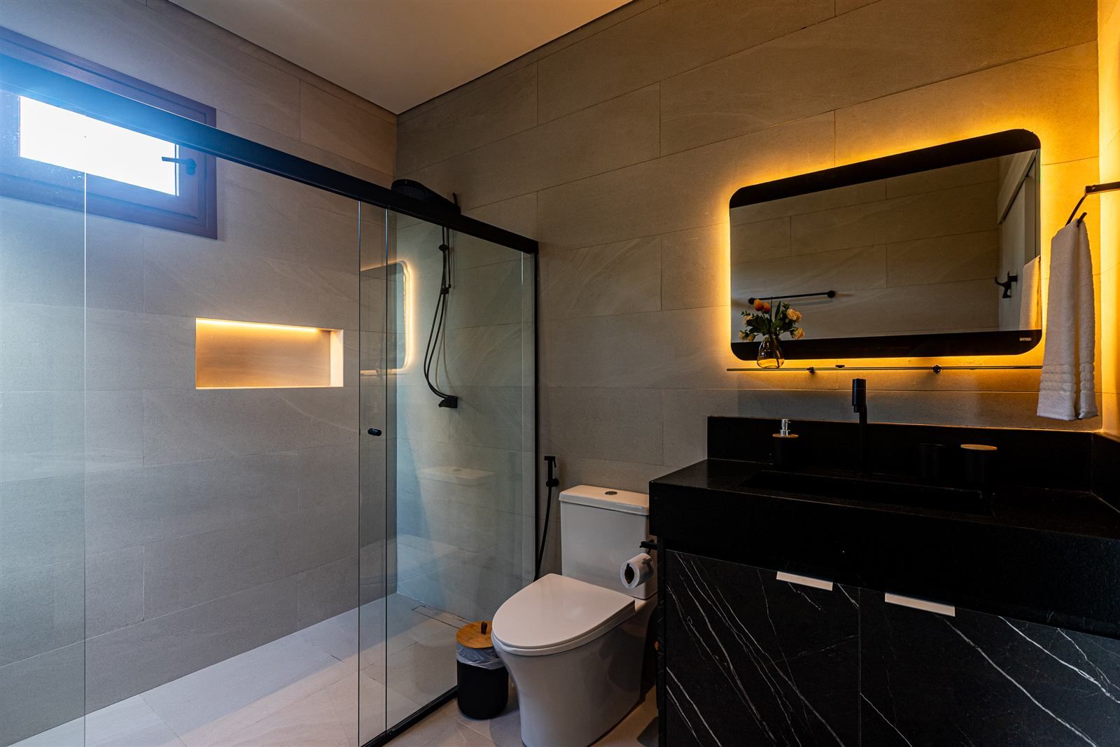 Een moderne badkamer met een douchecabine van glas, een toilet en een wastafel van zwart marmer.