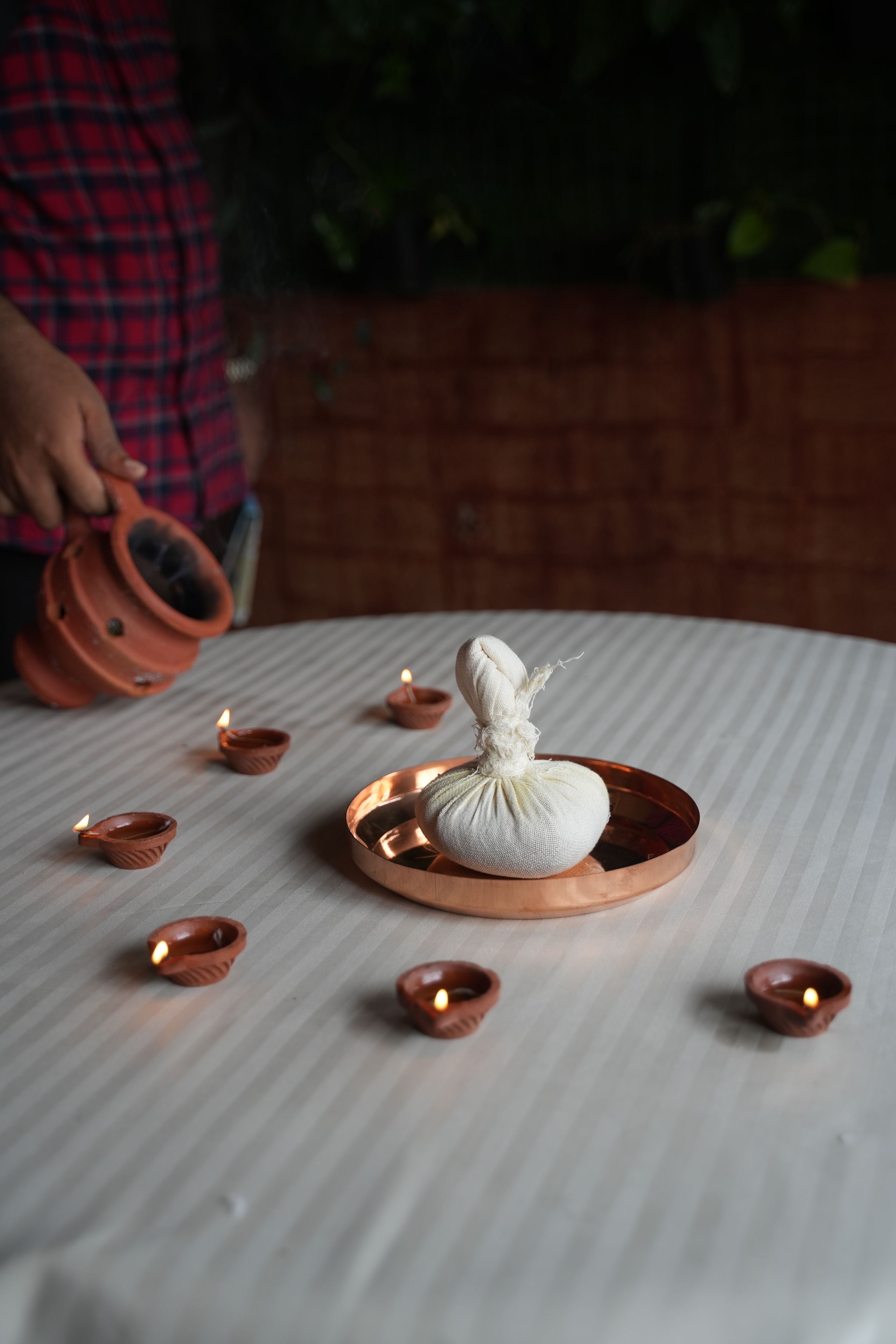 A table with a copper tray holding a white cloth, surrounded by small clay lamps.
