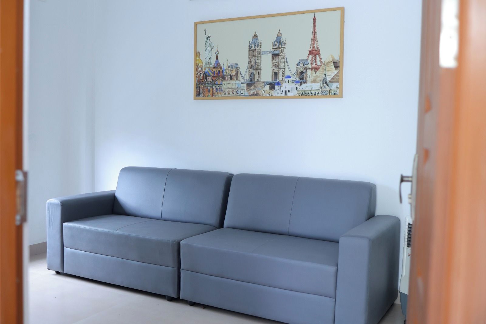 A grey sofa in a room with a white wall and a painting of a cityscape above it.
