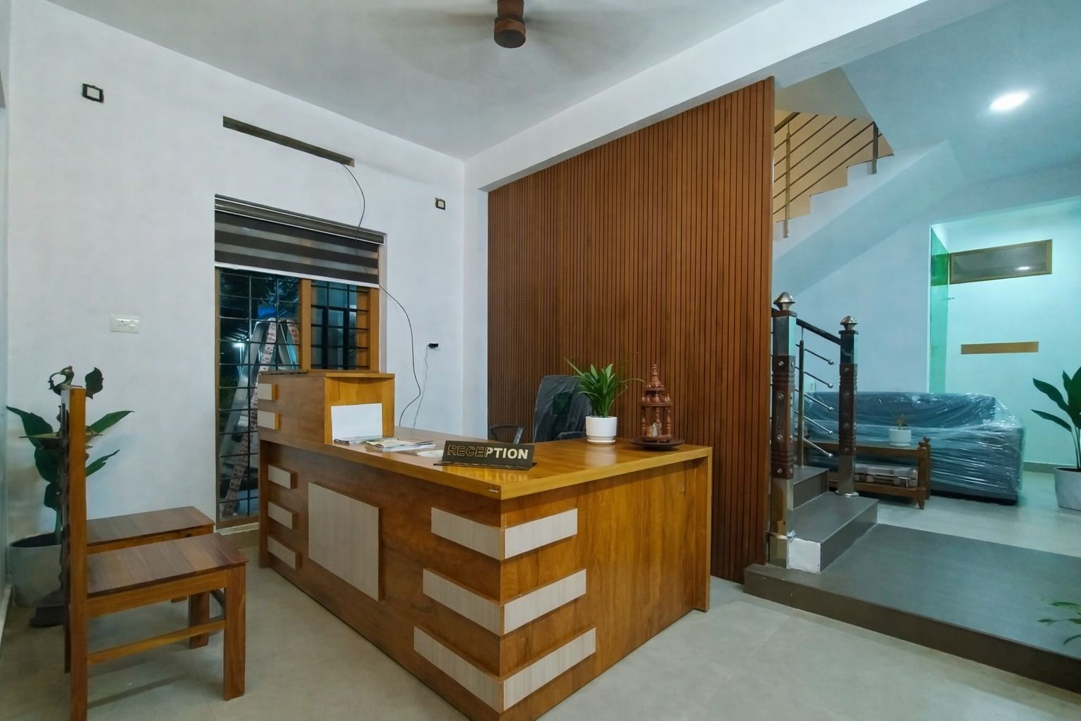 A reception desk with a wooden finish, a chair, and a potted plant.