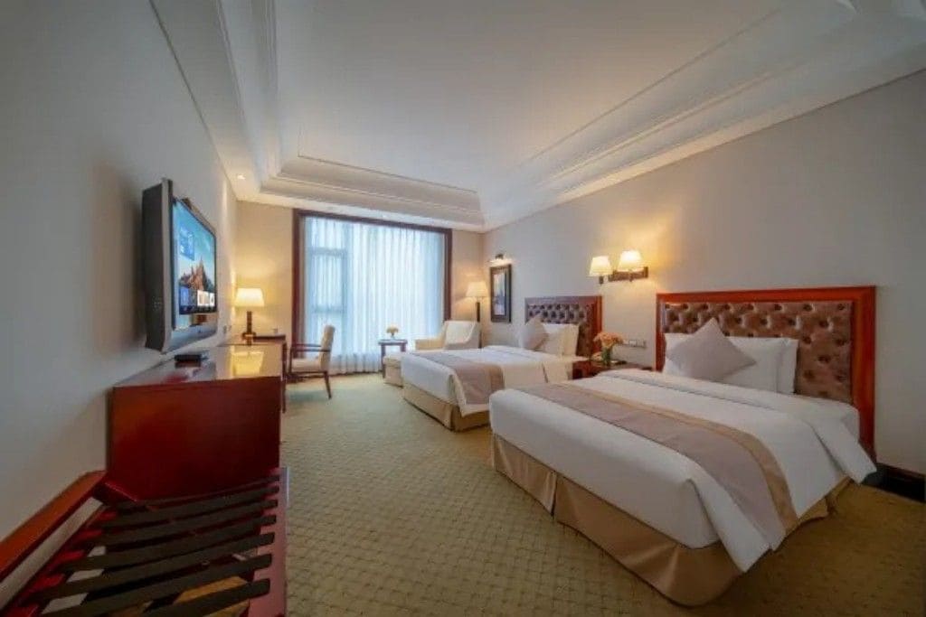 Habitación de hotel con dos camas, un escritorio, una silla, un televisor y una ventana con cortinas.