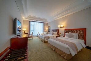 Ein Hotelzimmer mit zwei Betten, einem Schreibtisch, einem Sessel, einem Fernseher und einem Fenster mit Vorhängen.