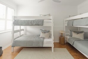 A bunk bed room with a white ceiling fan, a small wooden side table, and a window with blinds. - Beachfront, Pool, Games Room, Sleeps 12 (Henley Beach)