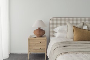 Et soveværelse med en seng, et natbord med en lampe og en ensfarvet væg.