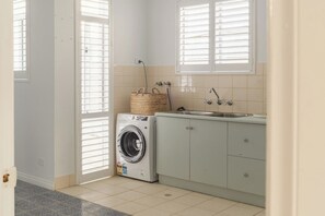 A laundry room with a washing machine, a sink, and cabinets. - Beachfront, Pool, Games Room, Sleeps 12 (Henley Beach)