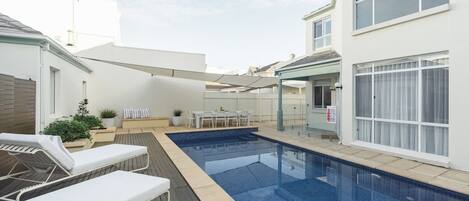 A swimming pool with lounge chairs, a table, and a covered seating area.