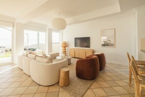 Una sala moderna con un sofá seccional, una mesa de centro de madera, un televisor y un comedor con sillas de madera.