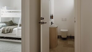 Un couloir menant à une chambre avec un lit superposé et une salle de bain équipée de toilettes et d’un lavabo.