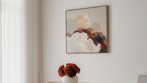 Un coin repas avec une table ronde, deux chaises, un vase de fleurs et un tableau accroché au mur.