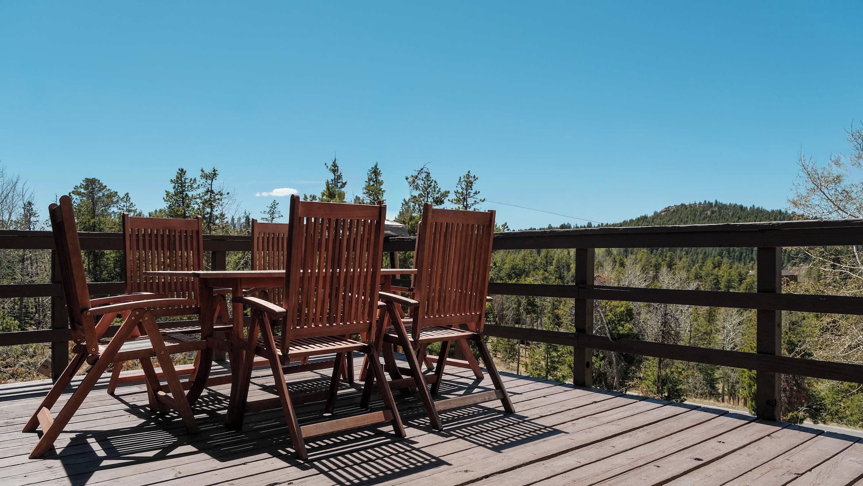 A wooden deck with a table and chairs, overlooking a forested landscape.