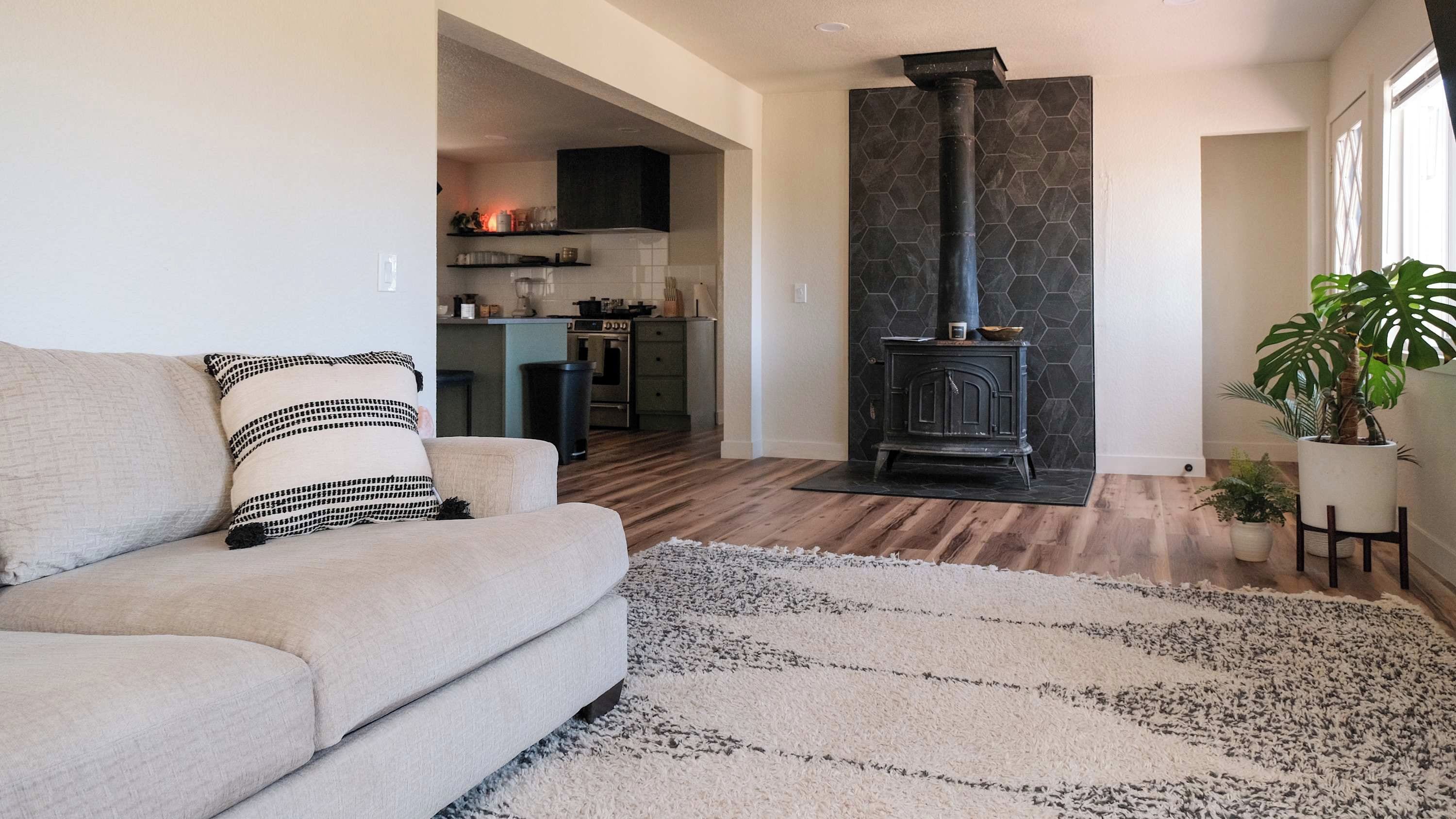 A living room with a sofa, a rug, a fireplace, and a kitchen in the background.