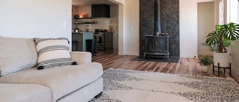A living room with a sofa, a rug, a fireplace, and a kitchen in the background.