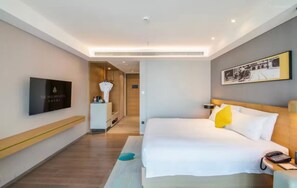 A hotel room with a bed, a bedside table with a phone, a TV on the wall, and a painting above the bed. - The Mulian Hotel Jinhai Lake Shanghai (Shanghai)