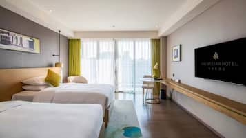 Habitación de hotel con dos camas, un escritorio, una silla, un televisor y una ventana con cortinas.