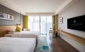 A hotel room with two beds, a desk, a chair, a TV, and a window with curtains.