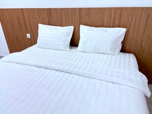 A bed with a wooden headboard, white bedding, and a power outlet on the wall.