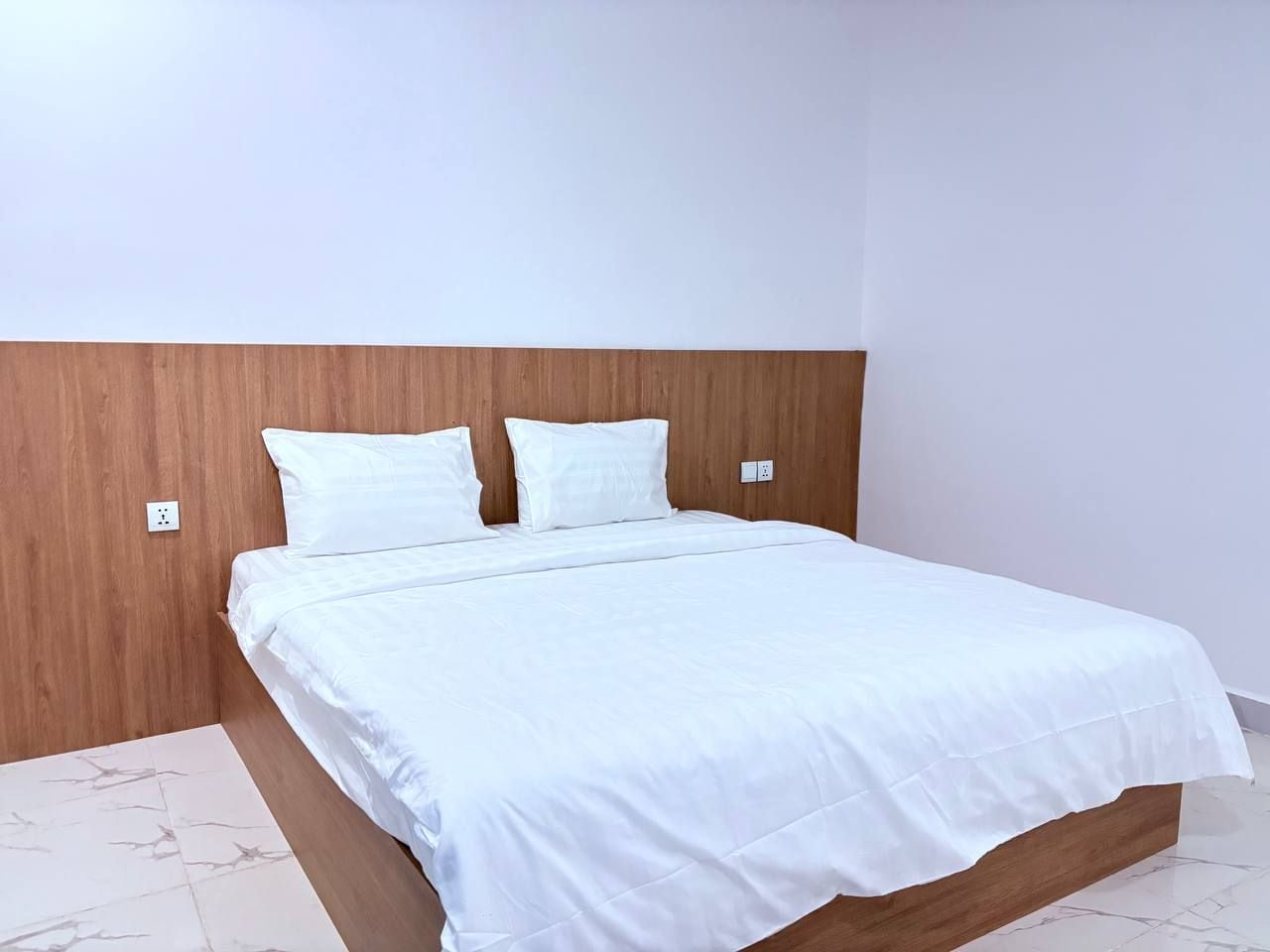 A bed with a wooden headboard, white bedding, and a white floor.