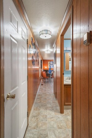 A hallway with wooden paneling, a tiled floor, and a dining area with a table and chairs. - Trainmaster's Inn - Tiny House (Palmer)