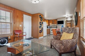 A compact living space with a kitchenette, a dining area with a glass table, and a patterned armchair. - Trainmaster's Inn - Tiny House (Palmer)