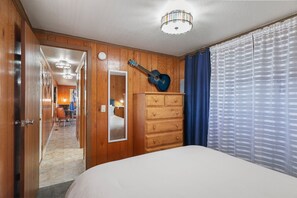 A hotel room with a bed, a dresser, a guitar, and a view of the hallway. - Trainmaster's Inn - Tiny House (Palmer)