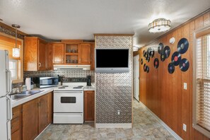 A compact kitchen with wooden cabinets, a built-in stove, and a flat-screen TV. - Trainmaster's Inn - Tiny House (Palmer)