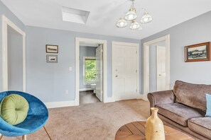 Ein Wohnzimmer mit einem braunen Sofa, einem blauen Sessel, einem Holztisch und einer Vase. Zwei Türen führen in andere Räume.