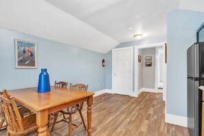 Ein Essbereich mit einem Holztisch und Stühlen, einer blauen Wasserflasche und einem alten Plakat eines Schneeglöckchen-Zuges an der Wand.