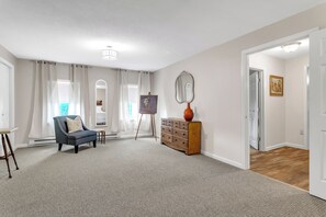 Ein geräumiges Wohnzimmer mit einem grauen Sessel, einer Holzkommode und einem Gemälde auf Staffeleien.